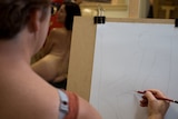 A student sketches a life art model.