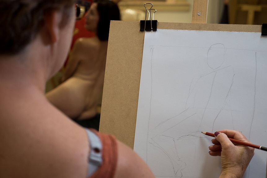 A student sketches a life art model.
