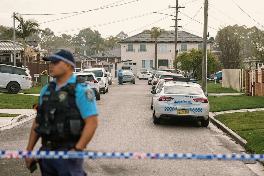 A police officer stands guard near tape in a street lined with police cars