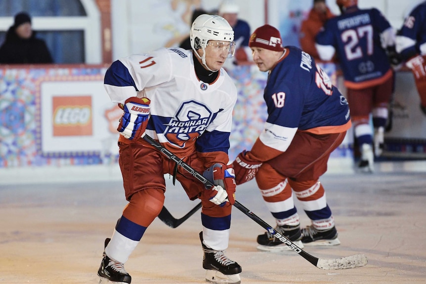 Russian president Vladimir Putin wearing a helmet and uniform, skates on ice with a hockey stick