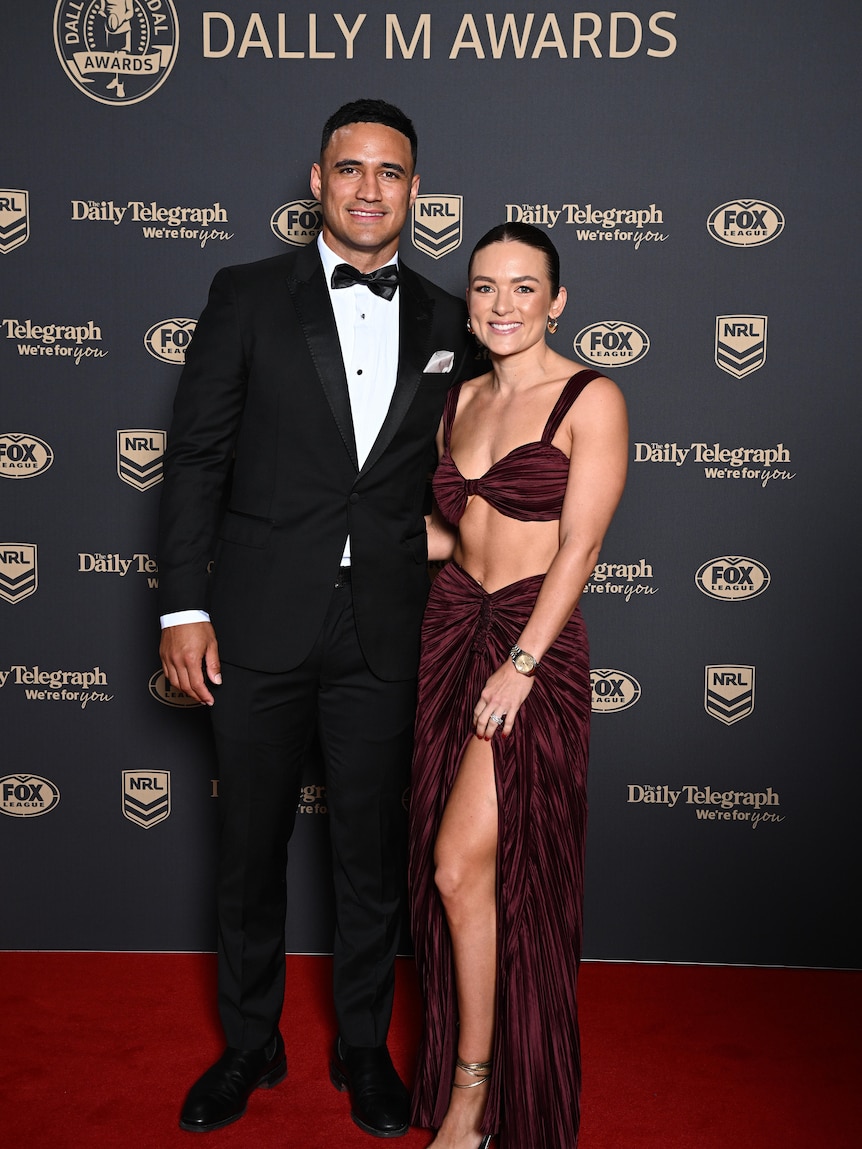 A man in a suit and a woman in a deep red dress pose on the red carpet. 