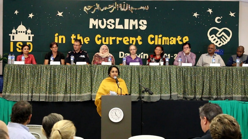 A panel of politicians, police and Muslim community leaders sit at a long table on a stage at an anti-discrimination meeting.