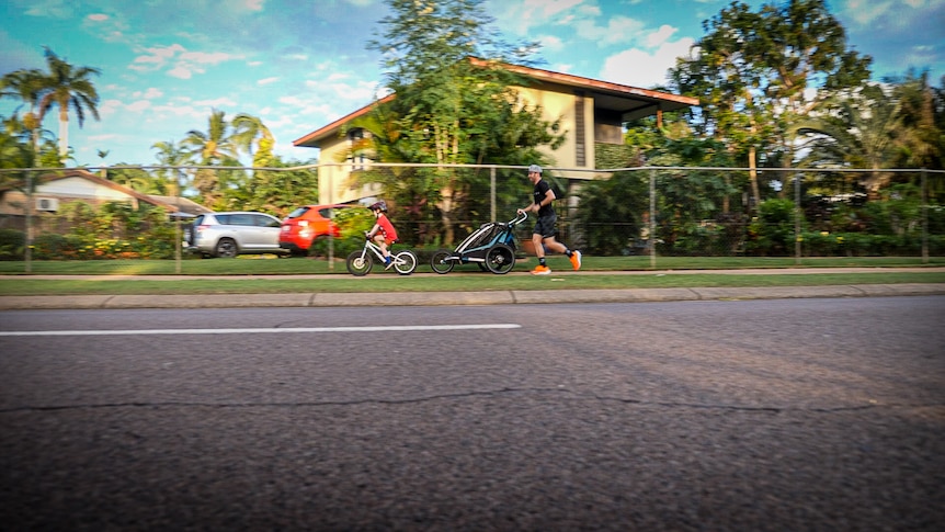 Street view across the road of family riding and running to school in a tropical suburb.