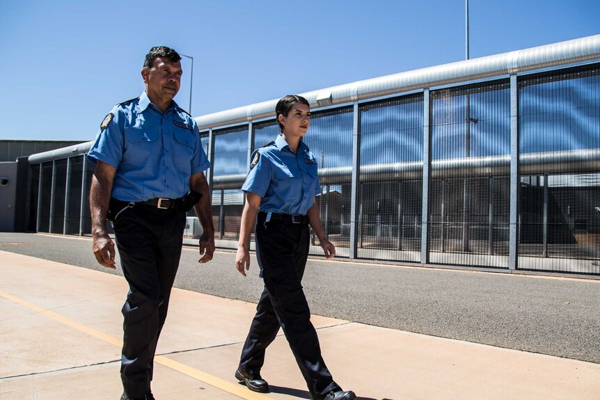 Two prison guards in uniform walking along the fence line at a jail.