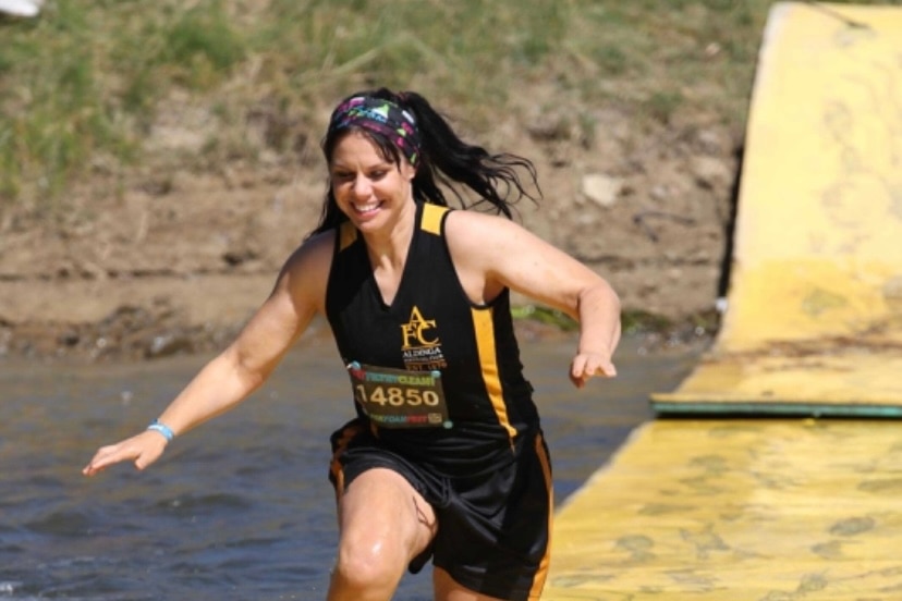 A woman runs along an inflated mat competing in a racing event along the water. 