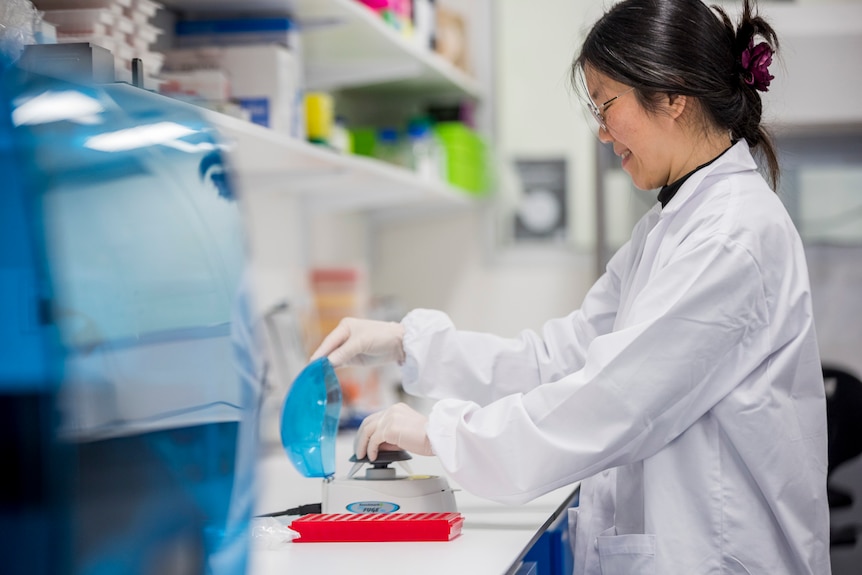 A woman wearing a science lab coat testing a water sample for DNA 