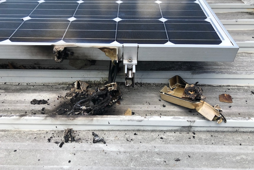 A solar panel on the roof of a home, where an exploded isolator lays burned and blackened