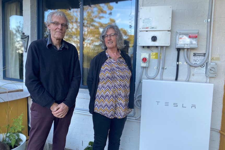two people stand in front of a Tesla battery unit
