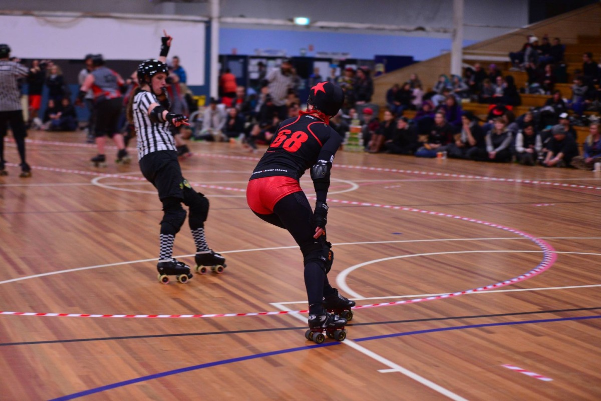 A woman on roller skates playing roller derby can be seen flying up the court.