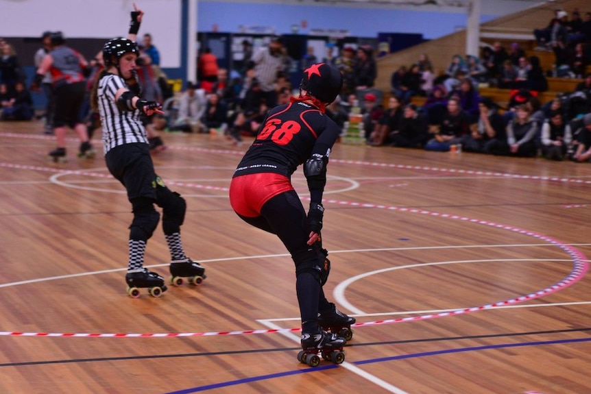A woman on roller skates playing roller derby can be seen flying up the court.