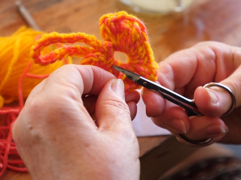 Close up of a crocheted heart being made and scissors cutting the thread.