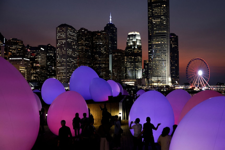 Large, soft egg-shaped artworks glow in pink and purple against the dusk skyline of Hong Kong.