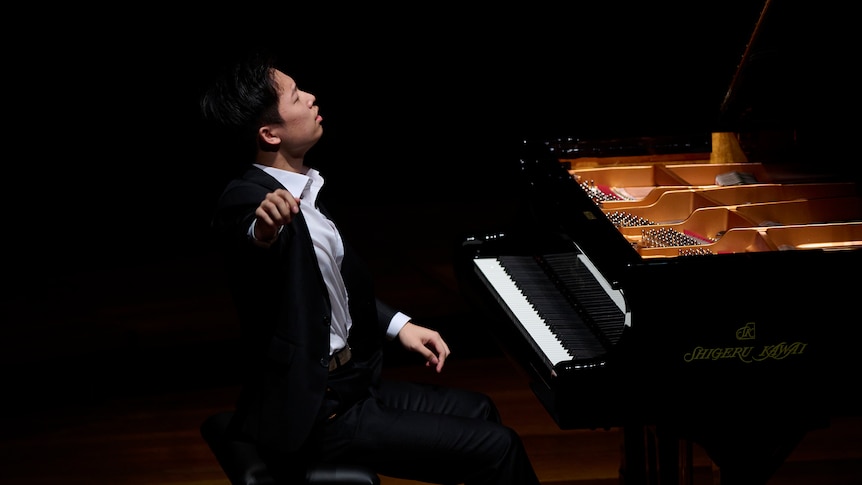 Jeonghwan Kim plays a grand piano. His head is thrown back and his right arm is flung out to the side.