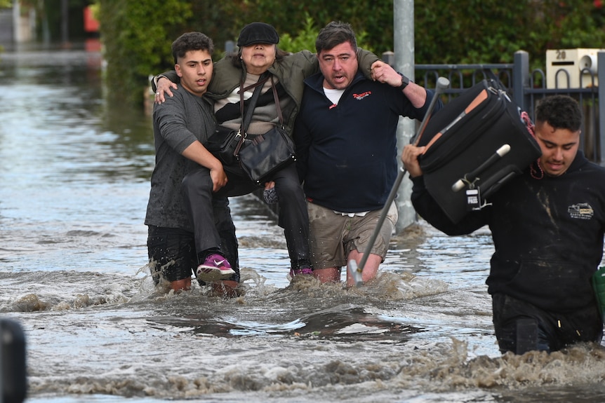 A woman is carried from floodwater by two men