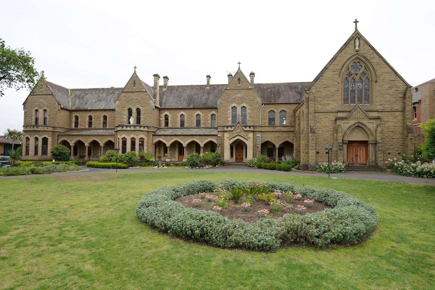 An old stone school building with a well manicured garden in the foreground.