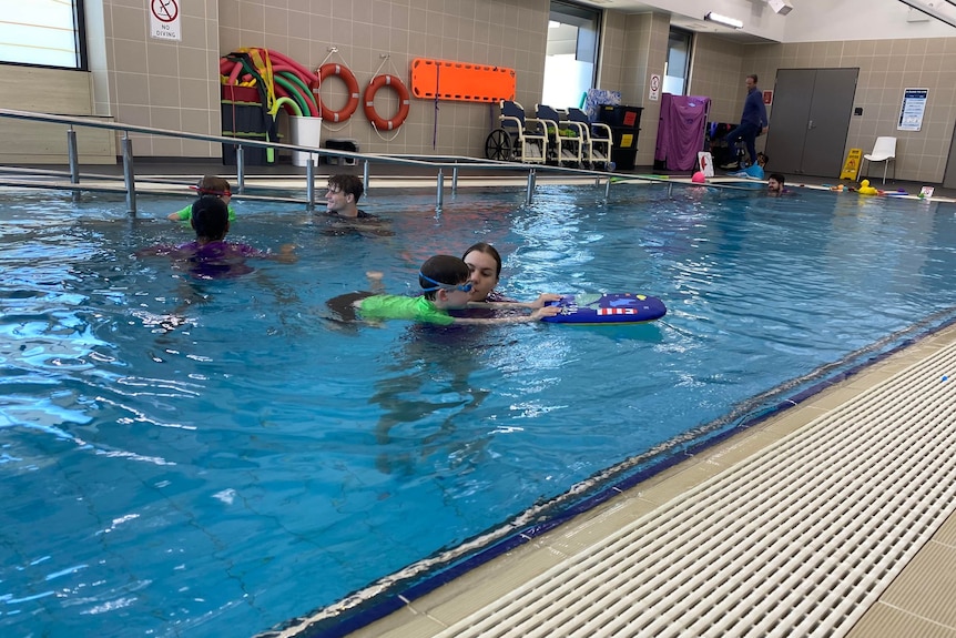 A child learns to kick with a kick-board in the pool.