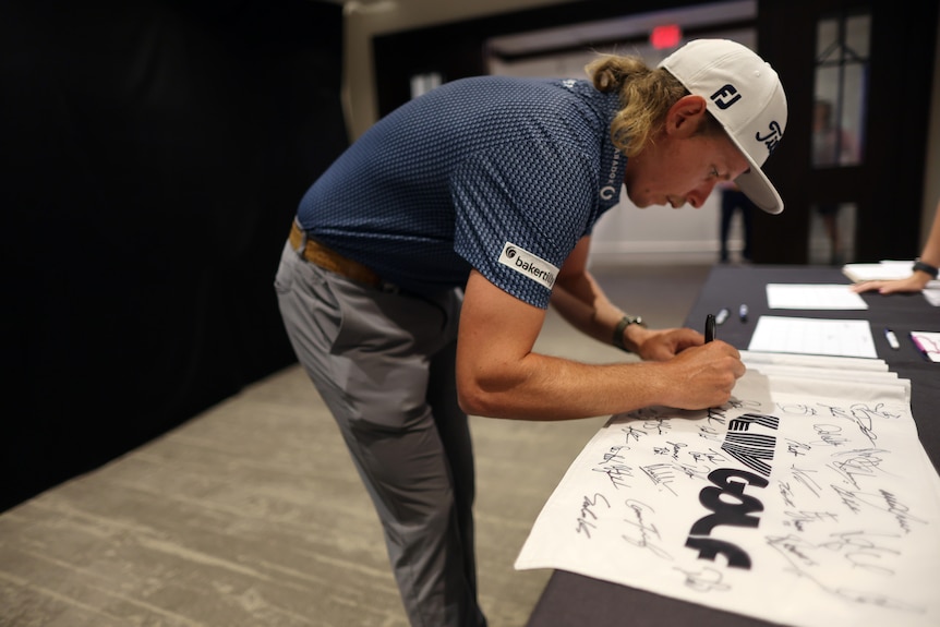 Cameron Smith signs a white sheet with LIV Golf written on it