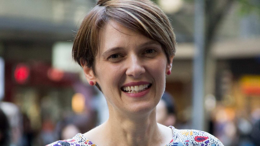 A woman looks at the camera, blurred city street in background.