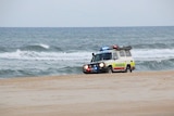 Ambulance four-wheel-drive vehicle driving on beach with surf in background on Fraser Island.