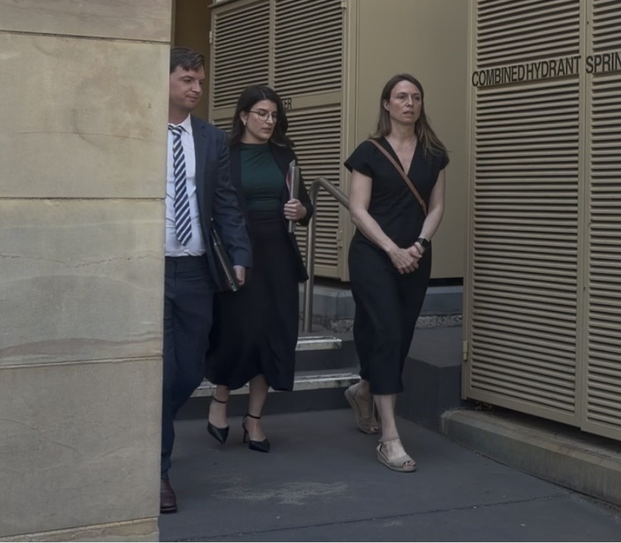 Dos mujeres y un hombre, todos vestidos de negocios, salen de un edificio con paredes beige