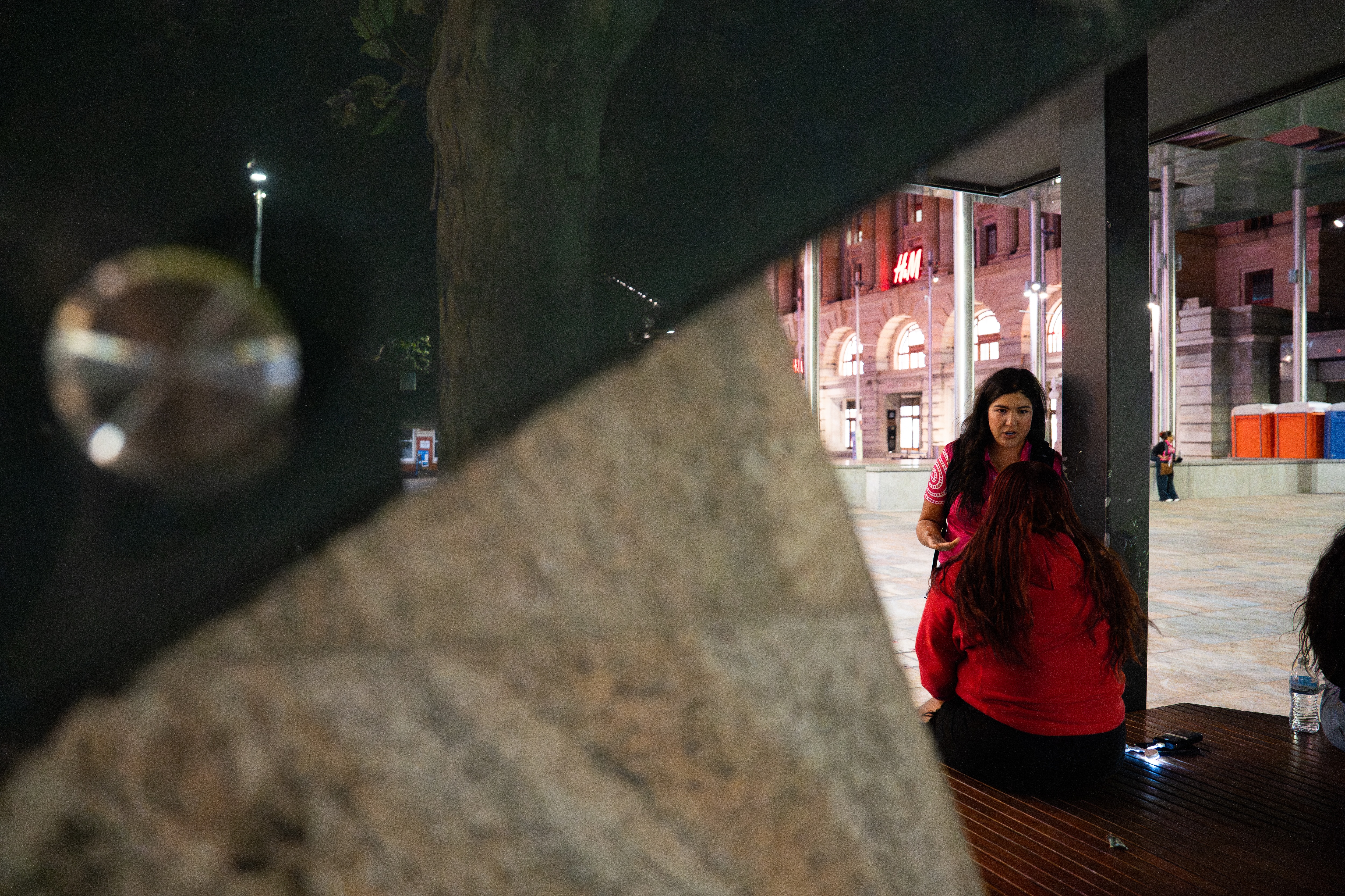 A female youth worker with long black hair talks to a teenage girl who is sitting down in Forrest Place.