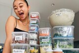 Food creator Liz Miu smiles behind a stack of clear food storage containers filled with food piled high.