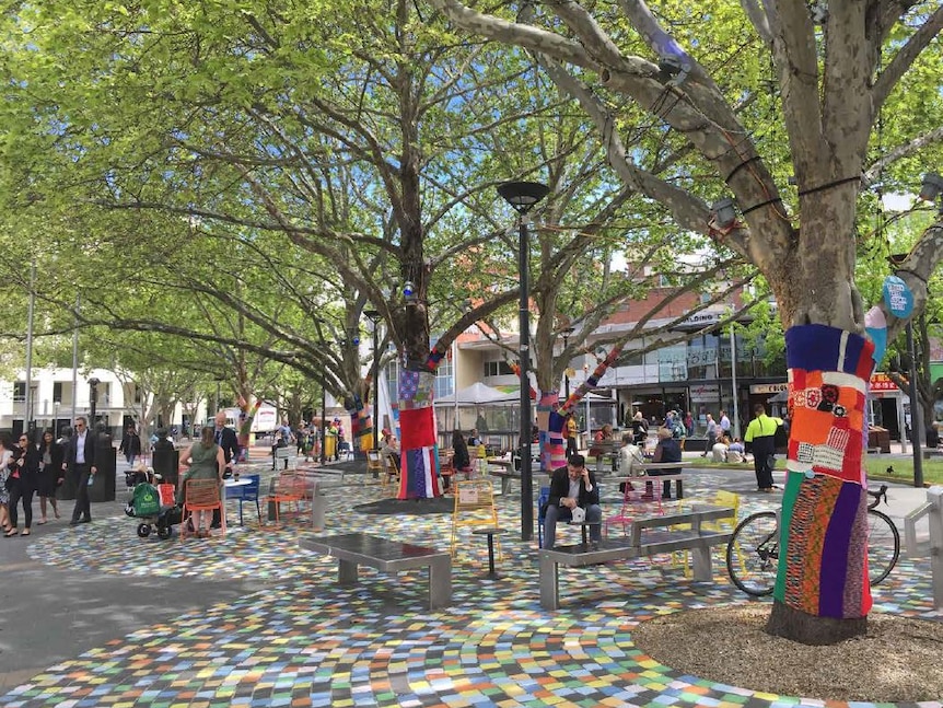 A plaza with colourful chairs, trees wrapped in colourful wool and painted pavement.