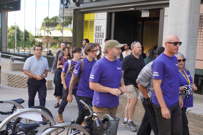 Staff in purple union shirts walk out of a university building
