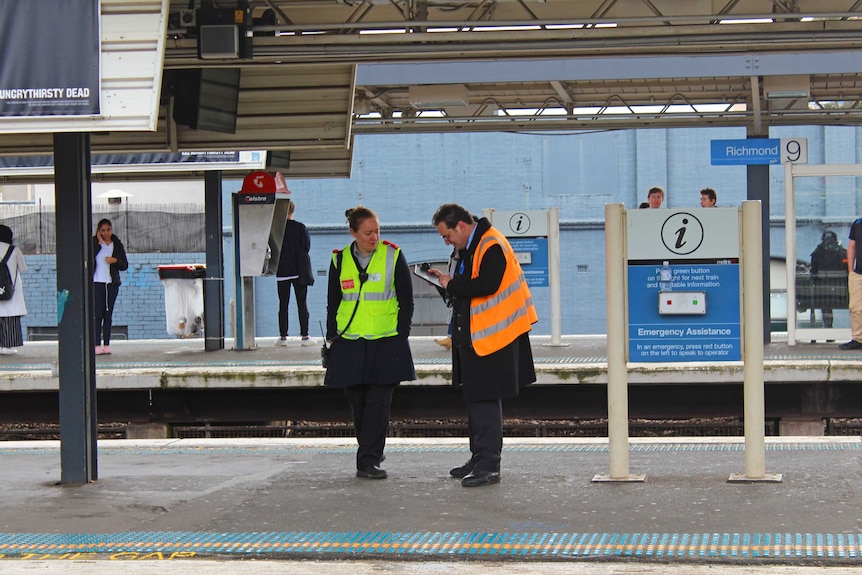 A man and a woman in high-vis vests stand on a train platform, with a sign that says "Richmond."