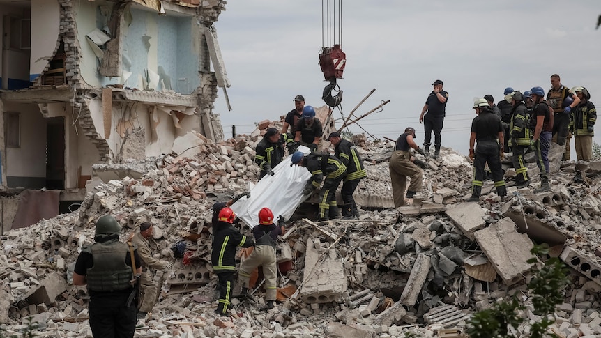 A team of people extract a body from a building damaged in a military strike