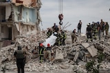 A team of people extract a body from a building damaged in a military strike