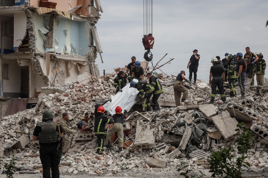 A team of people extract a body from a building damaged in a military strike