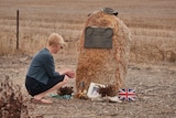 A woman kneels at a roadside memorial ahead