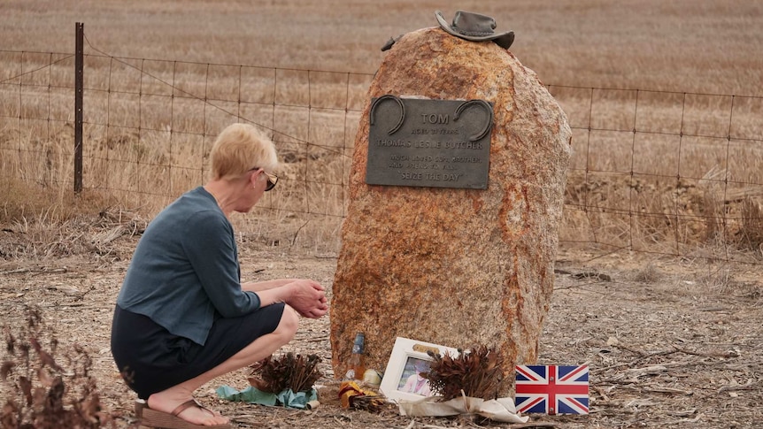 A woman kneels at a roadside memorial ahead