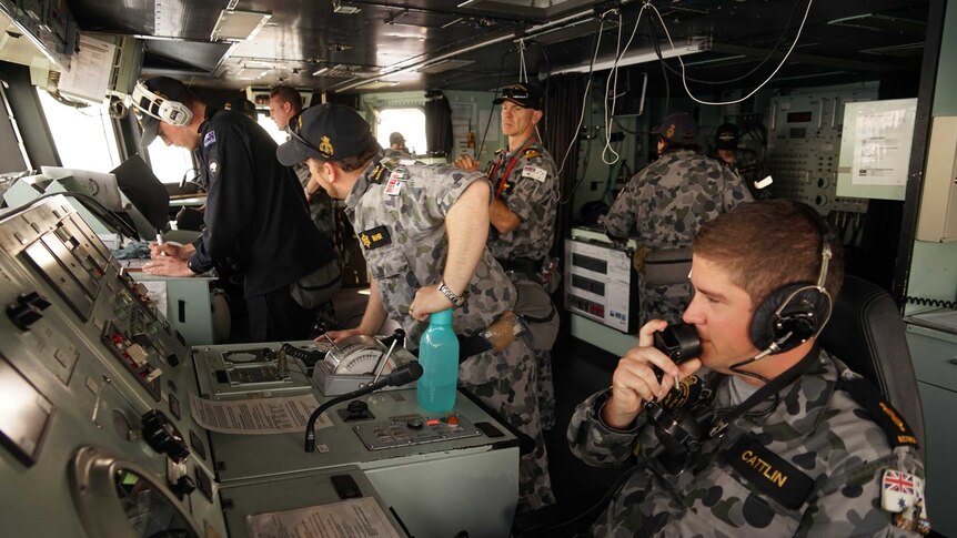 Navy personnel work on the bridge of a warship.
