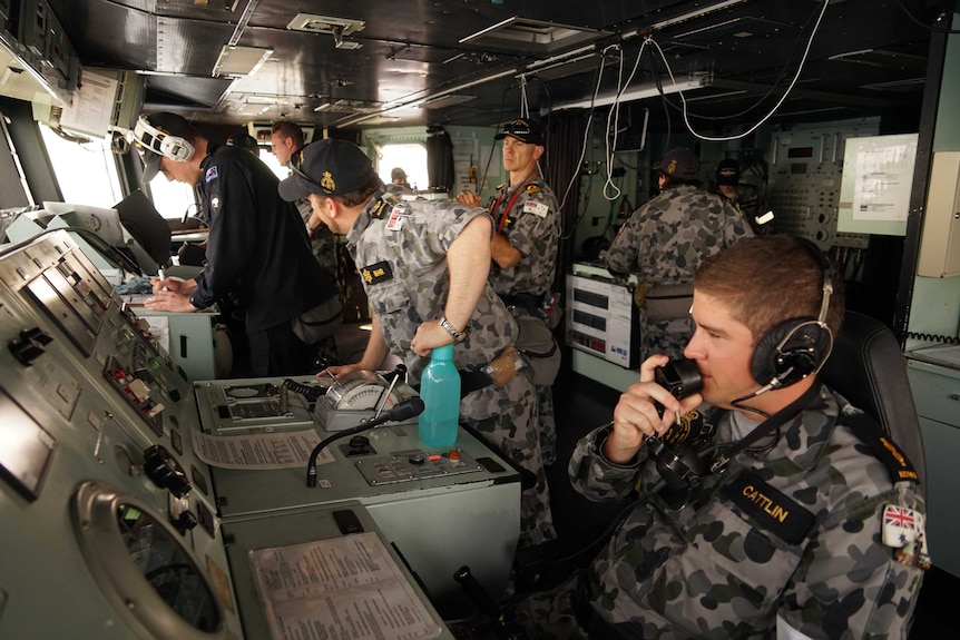 Navy personnel work on the bridge of a warship.