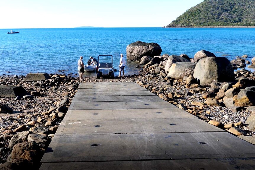 a cement boat ramp leading into the ocean, with men putting a boat in