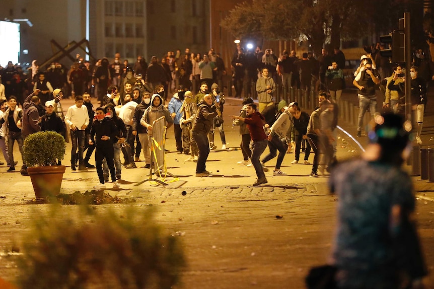 A large group of protesters are gathered across a road and are throwing items