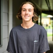 Young man with long hair standing in hallway.