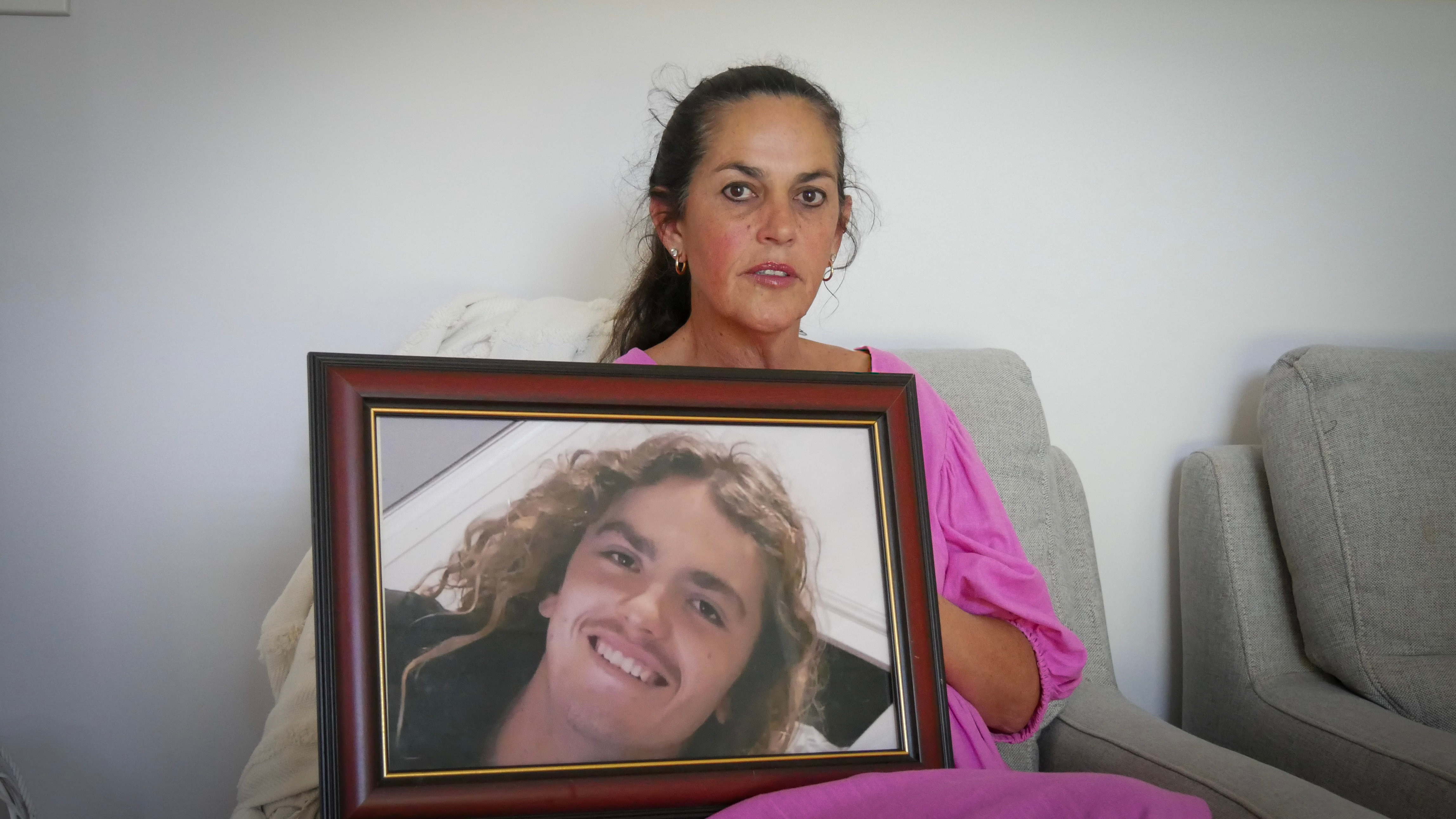 A woman sitting on a couch holding a large framed photo of her son.