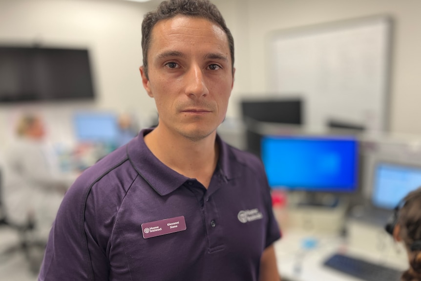 Giovanni wearing a purple Home Instead uniform shirt, looking at the camera with a serious expression.