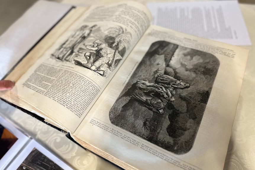 A bible sitting open on a table with detailed illustrations in black and white