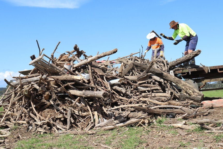 A pile of sticks, logs and plastic being cleared by two men in high-viz shirts.