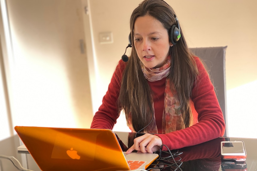 A woman with a headset on working at a laptop. 