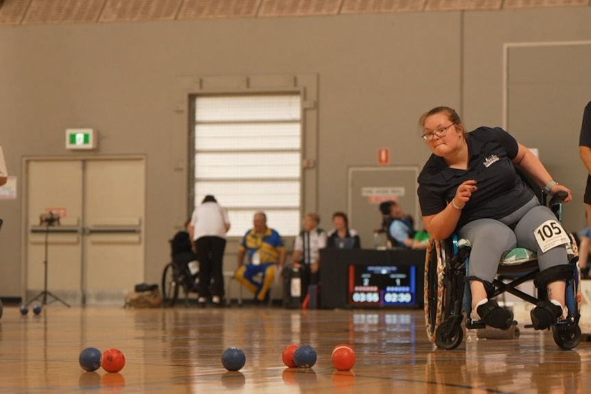Boccia player Jessi Hooper is sitting in her wheelchair looking at the court after throwing a ball.