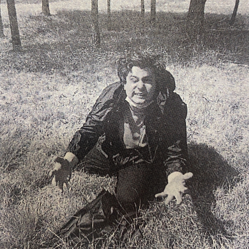 A black and white image of a man squatting down in a field.