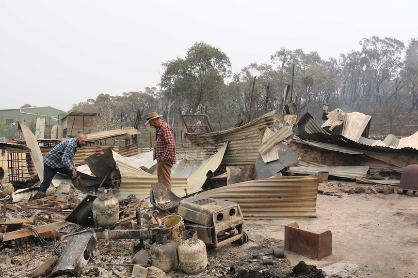 Two men pick through the remains of a destroyed home.