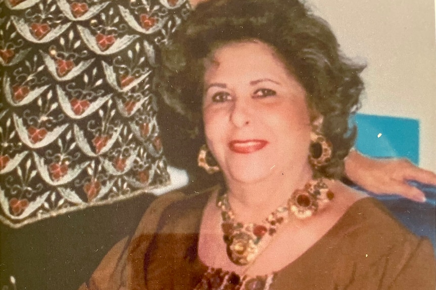 Old photograph of an older woman wearing a large gold, jewel-encrusted necklace and earrings smiling at the camera.