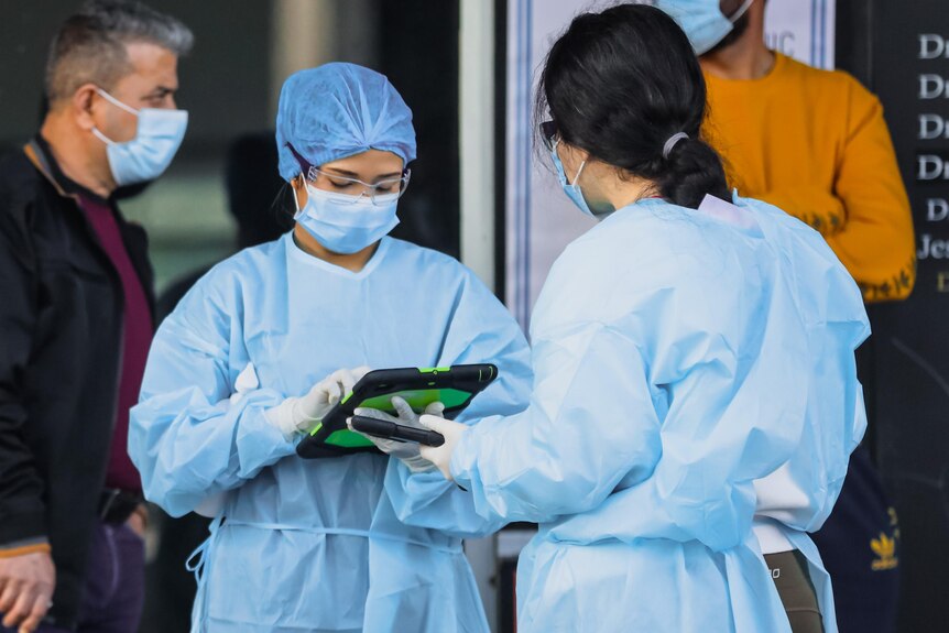 two women wearing protective clothing looking at a tablet