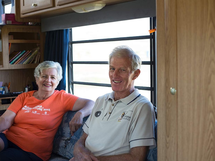 A couple sitting on a couch inside a motor home, smiling.